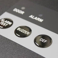 Example of embossed overlay label printing with three glossy buttons labeled “ALARM TEST,” “BUZZER,” and “DEF.”